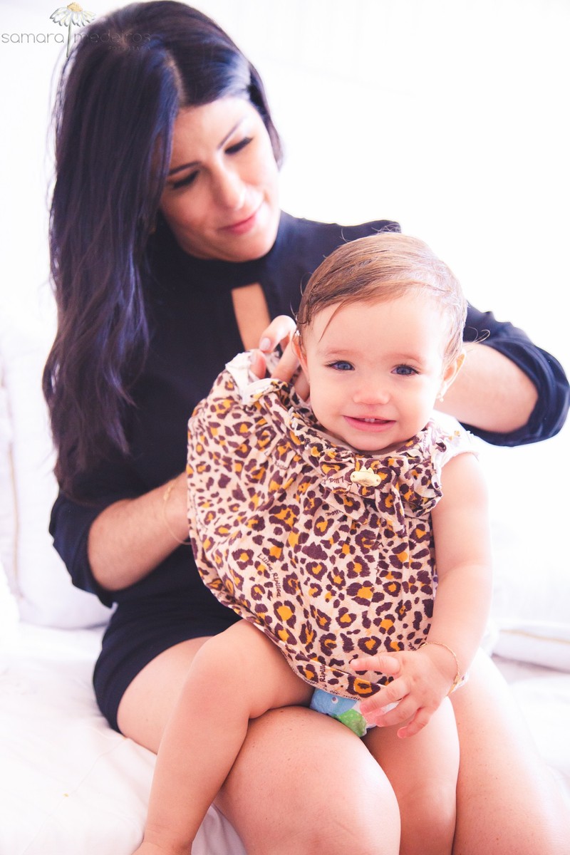 Mãe colocando um vestido em uma criança, enquanto ela olha para a foto e sorri.