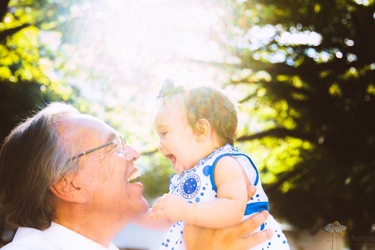 Pai brincando com criança, de jogar para cima, enquanto a criança gargalha, com o sol ao fundo dando reflexo.