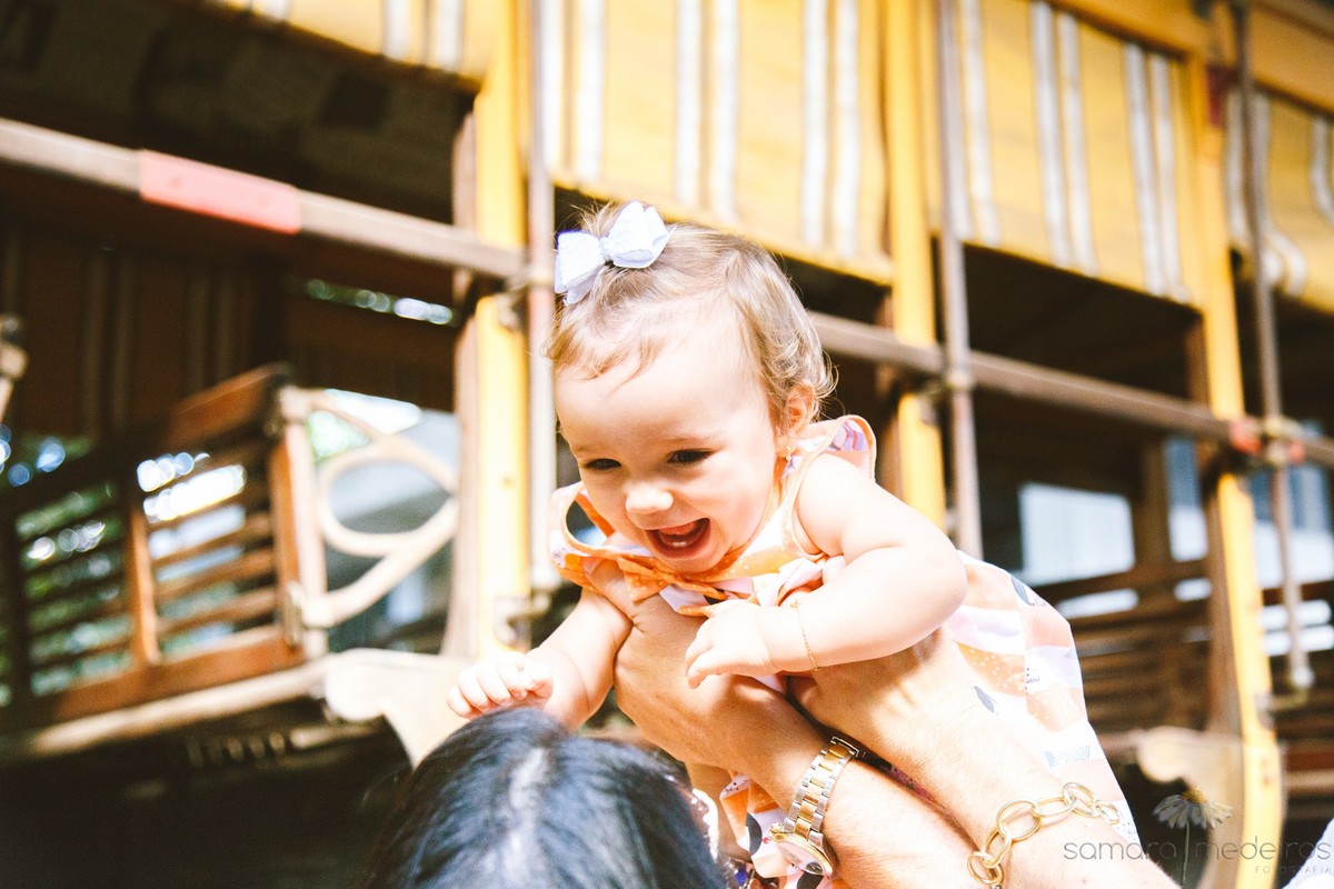 Mãe brincando de jogar criança para cima, foco na criança que ri, durante ensaio de fotos de sessão família.