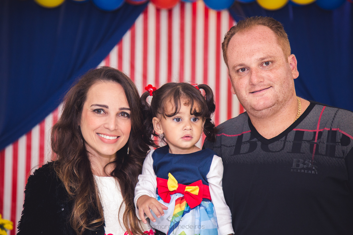 Foto dos pais com a criança em frente ao painel do tema da festa de aniversário de 2 anos.