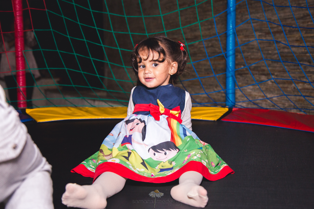 Criança sentada, após pular na cama elástica em festa de aniversário infantil.