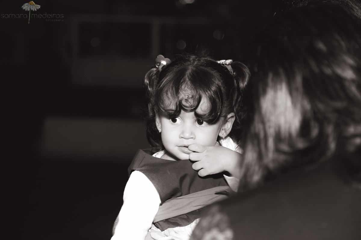 Foto em preto e branco de uma criança no colo de um adulto, com a mão na boca e uma expressão pensativa.