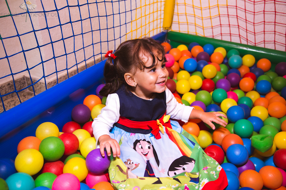 Criança brincando na piscina de bolinhas e sorrindo em sua festa de aniversário de 2 anos.