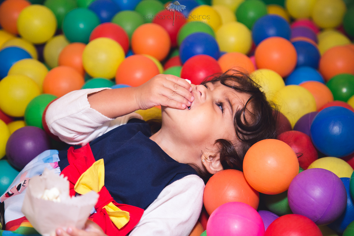 Criança comendo pipoca na piscina de bolinhas em sua festa de aniversário no salão do prédio.