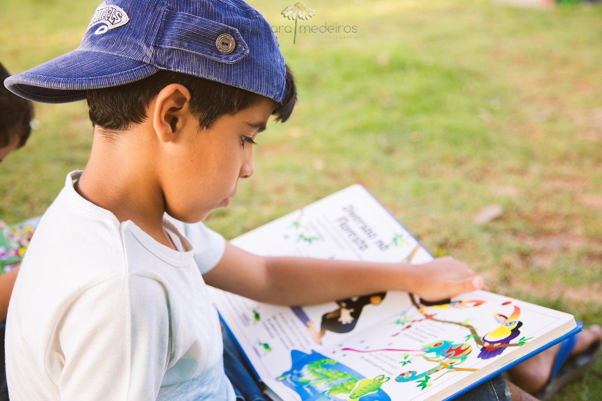 Menino com um livro aberto no colo, lendo, sentado na grama