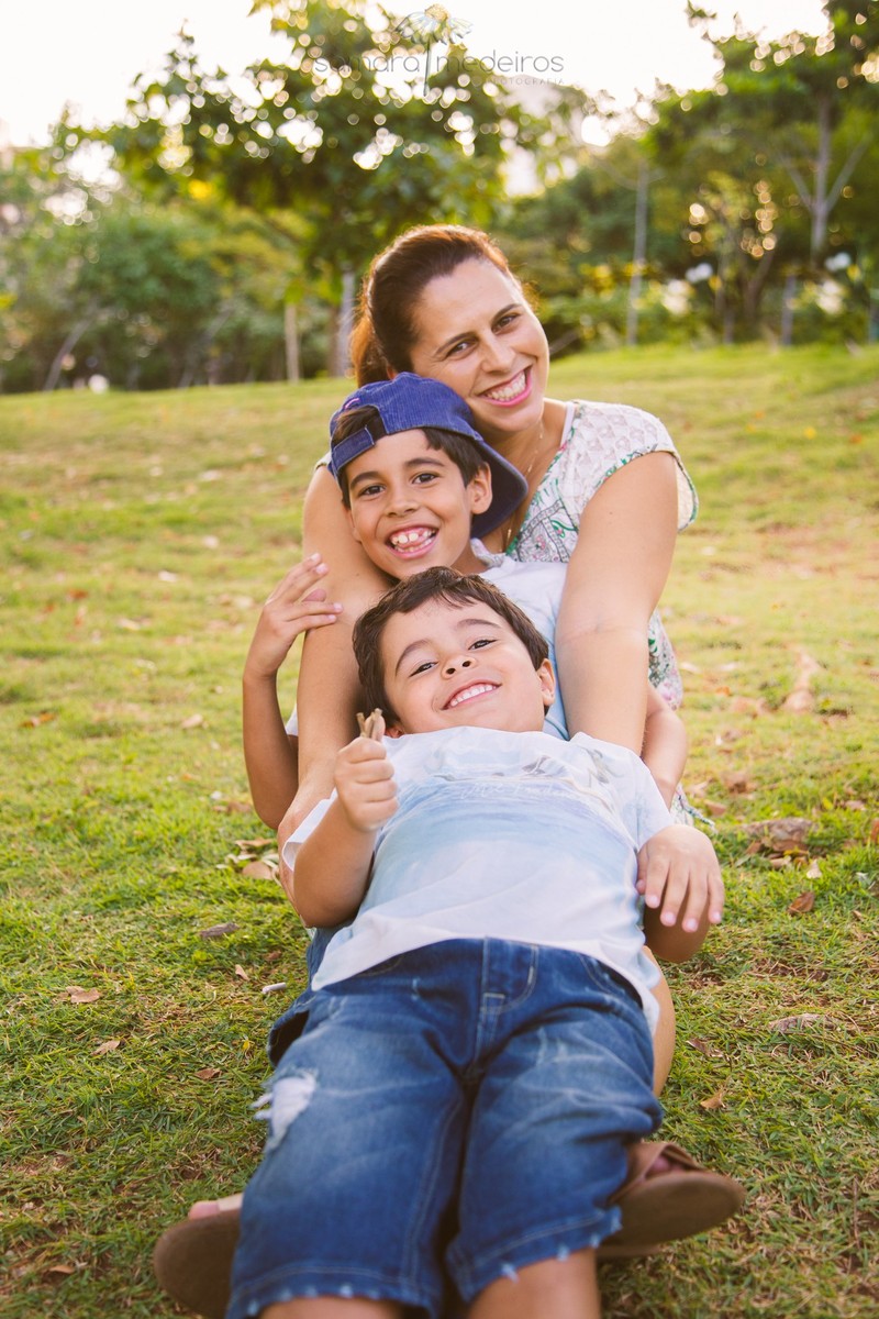 Mãe com seus dois filhos deitados em seu colo, formando uma escadinha, durante sessão de fotos de família em Belo Horizonte.