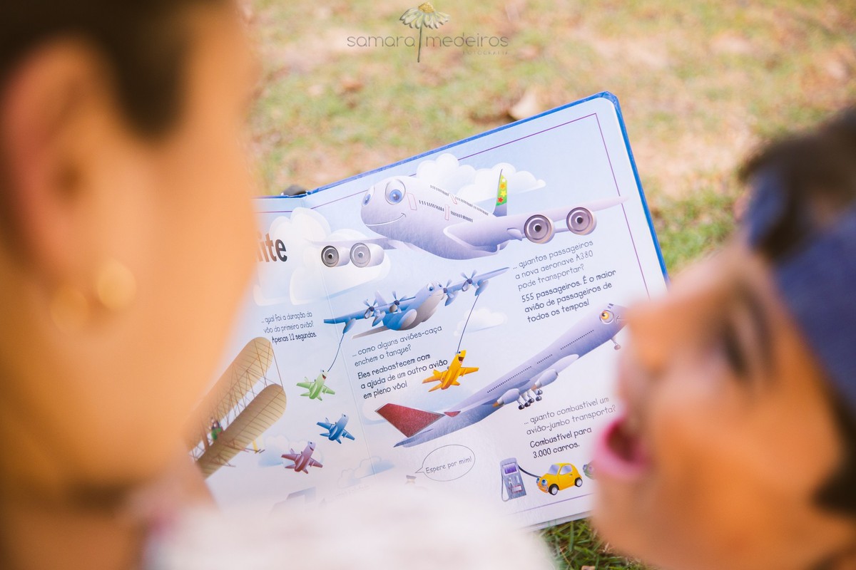 Mãe e seu filho em primeiro plano, desfocados, lendo um livro que aparece com foco em segundo plano, no colo deles.