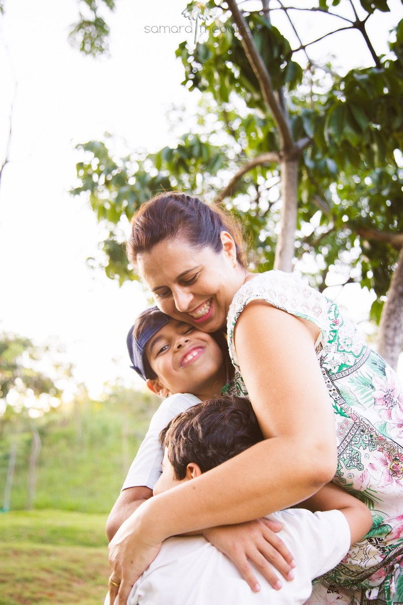 Mãe abraçando seus dois filhos em um parque, com árvores ao fundo, durante um ensaio fotográfico em Belo Horizonte.