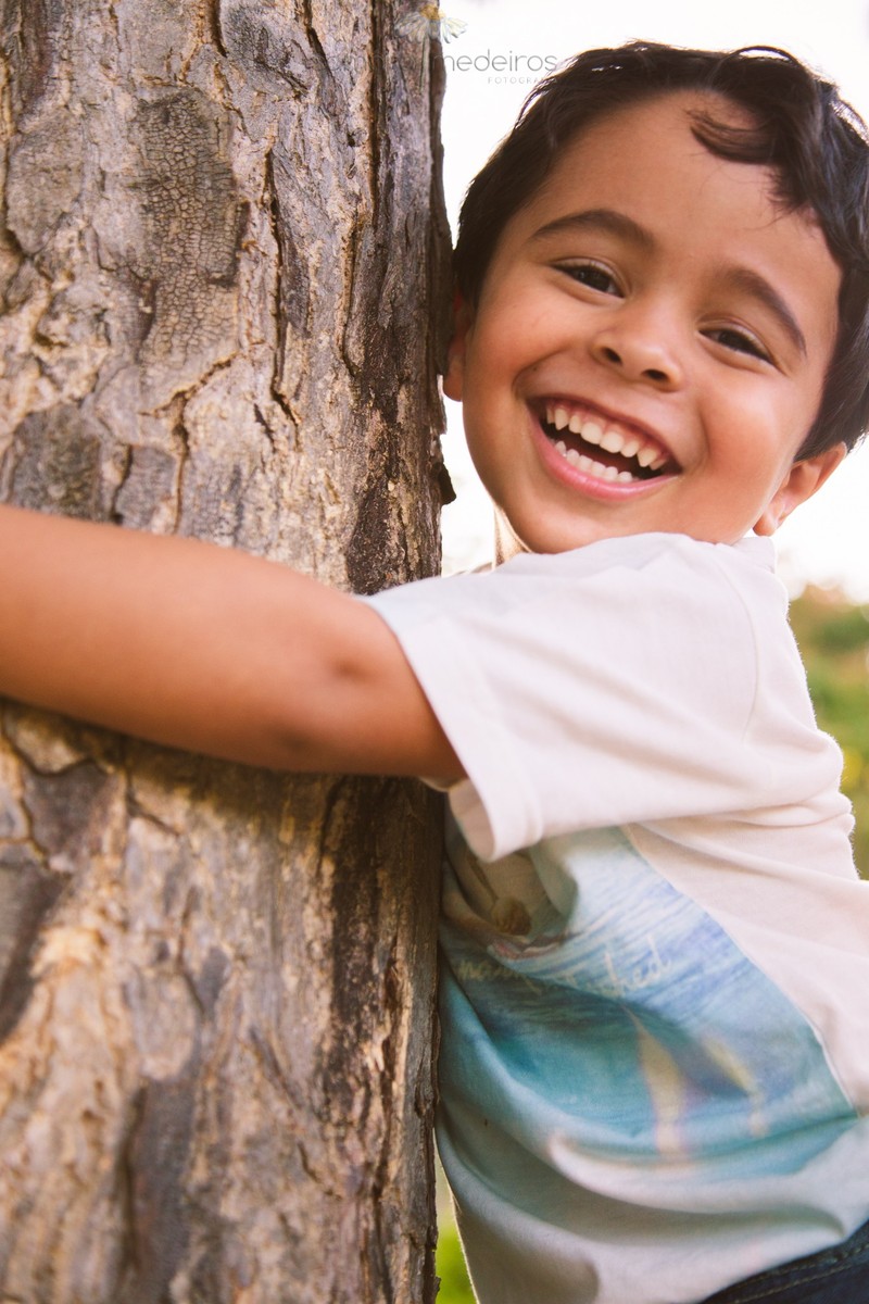 Criança agarrada a uma árvore e sorrindo para a foto.
