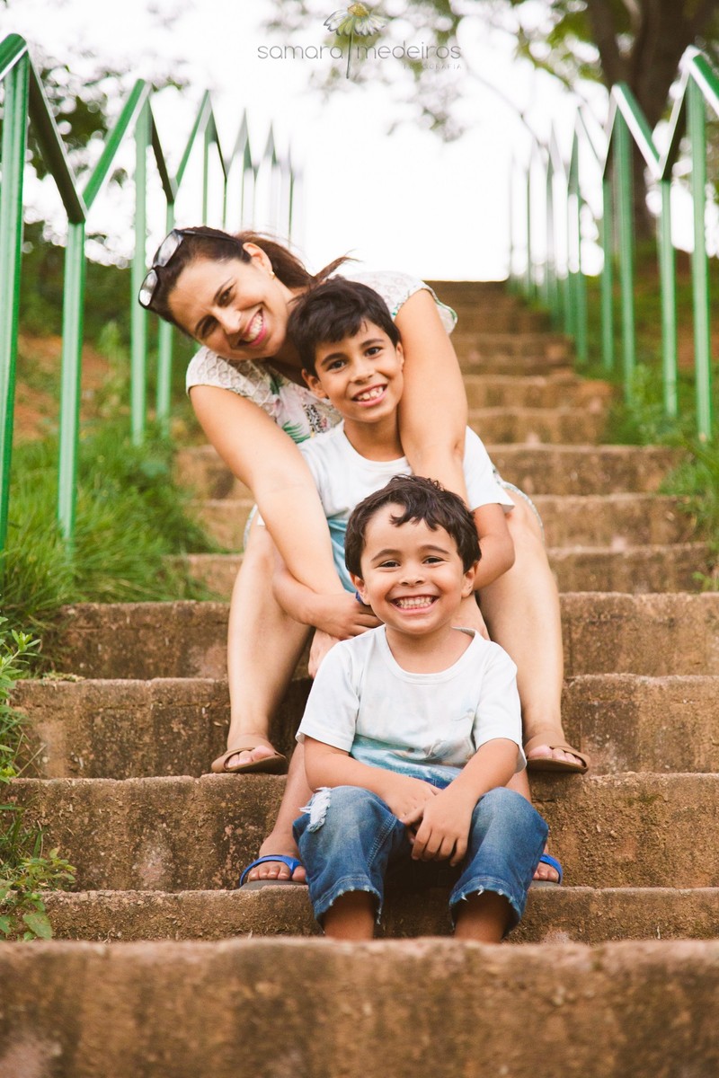 Mãe e dois filhos sentados em escadinha em uma escada de um parque de Belo Horizonte, posando para uma sessão de fotos de família.