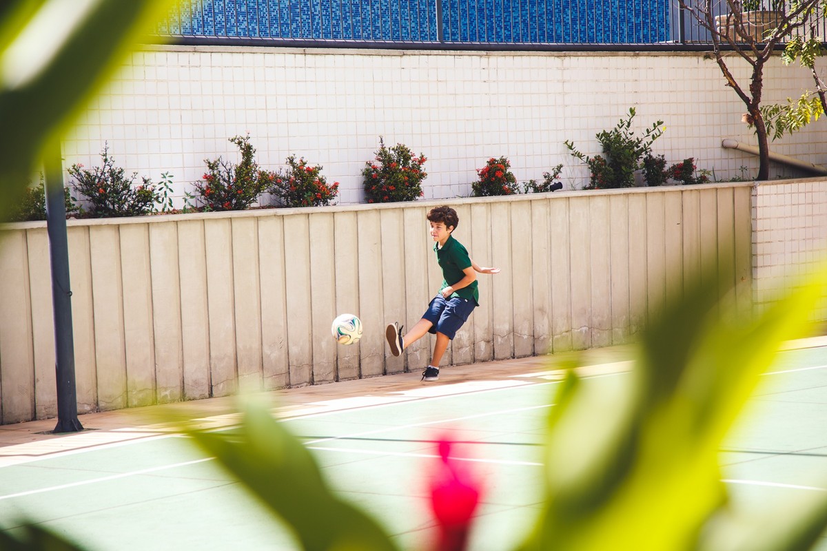 Criança jogando futebol durante aniversário infantil em um salão de festas de prédio.
