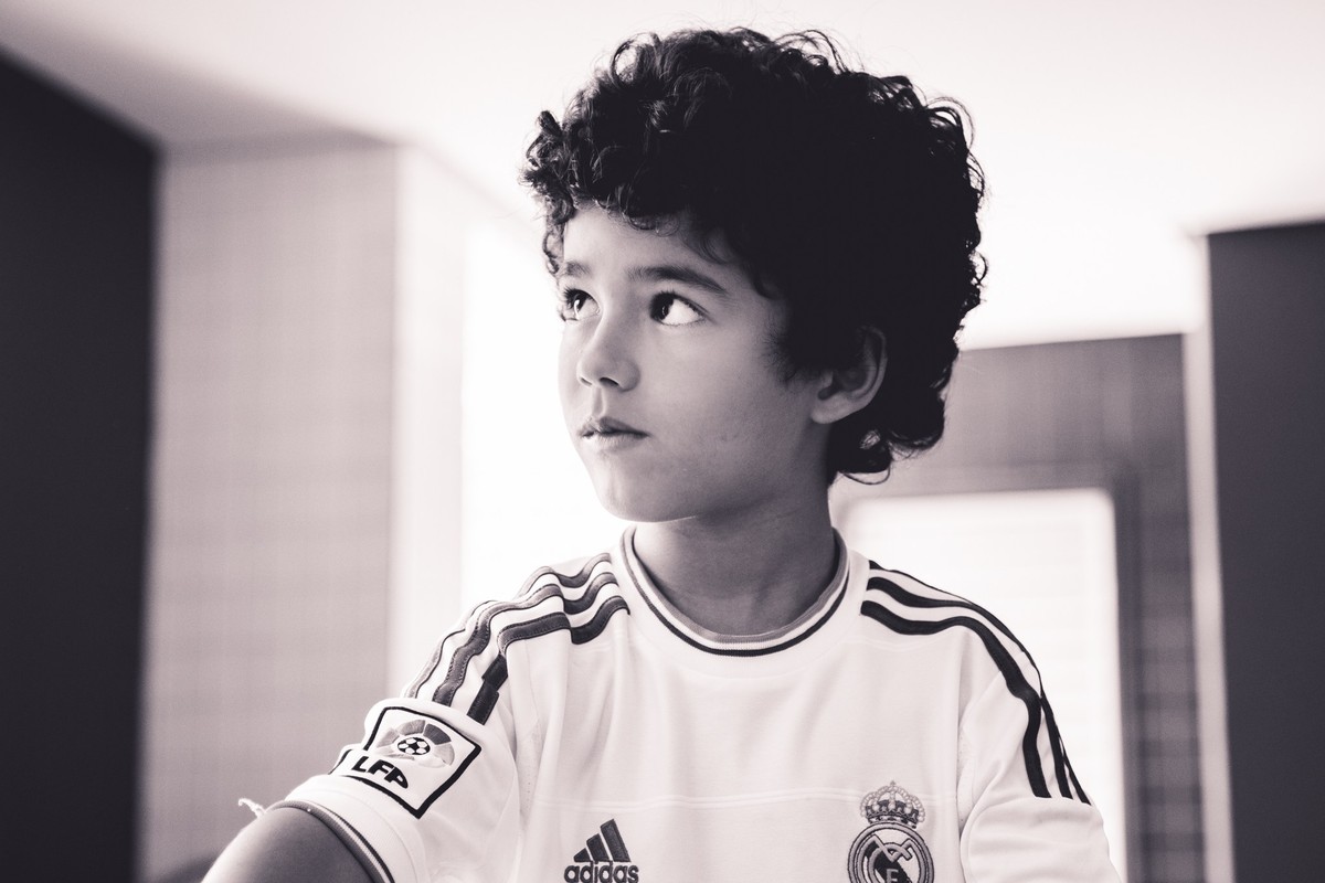 Foto em preto e branco de close em uma criança, enquanto ela observa algo ao lado.