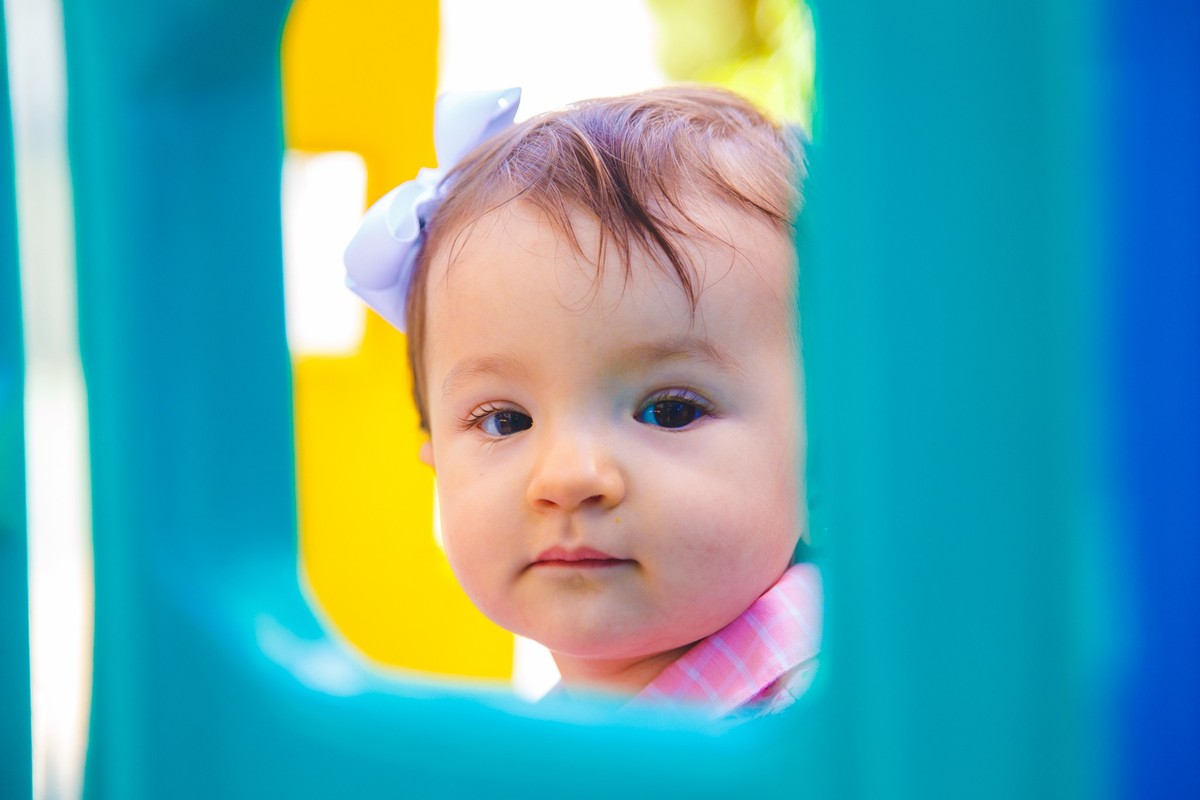 Close no rosto da criança emoldurada pelo brinquedo do parquinho do prédio, durante aniversário.