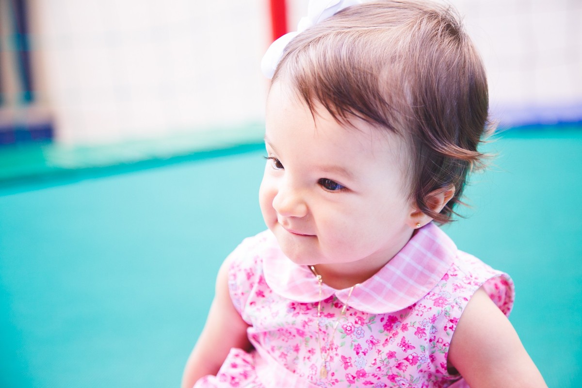 Criança sorrindo enquanto observa algo, sentada em uma cama elástica.