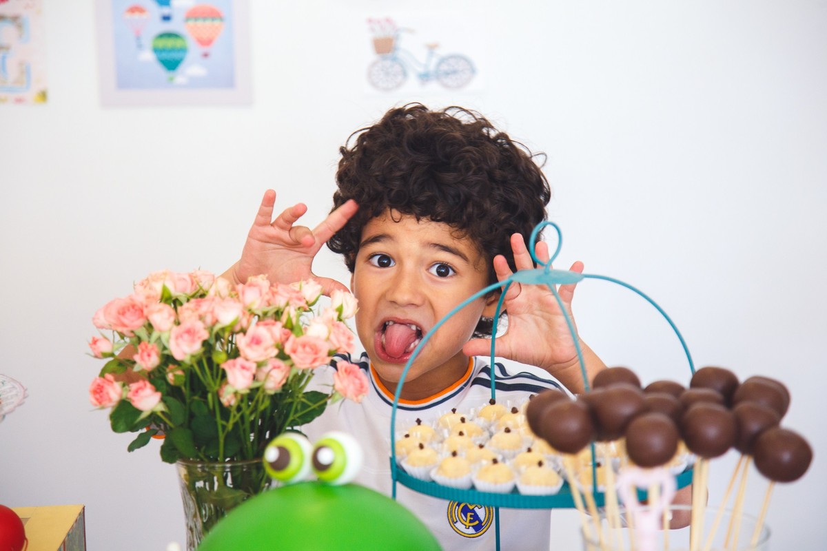 Criança atrás da mesa do bolo de uma festa de aniversário, fazendo careta de língua de fora para a câmera.