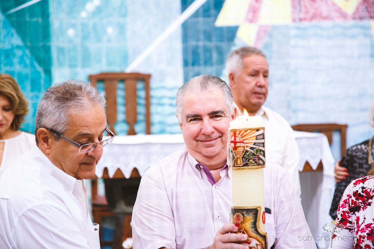 Avôs da criança segurando a vela para benção durante cerimônia de batizado em igreja de Belo Horizonte.