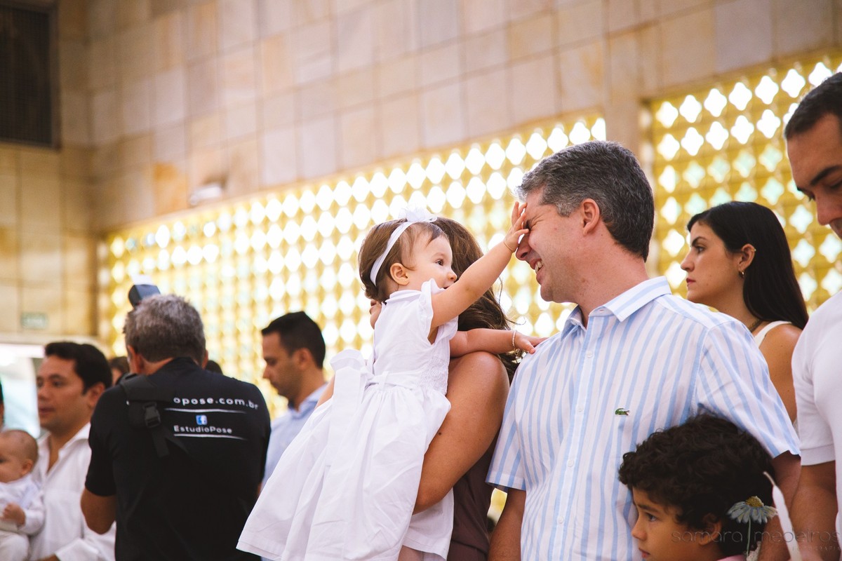 Criança brincando com o rosto do pai dentro da igreja durante seu batizado.