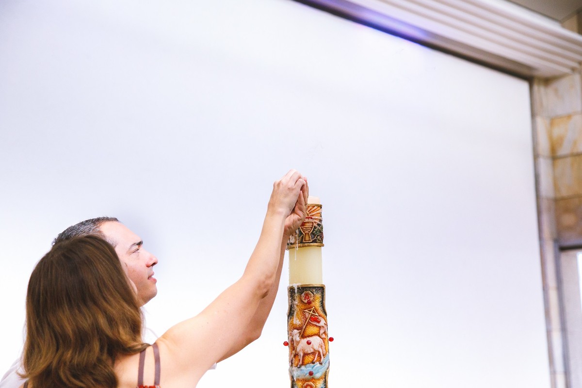 Padrinhos de batismo acendendo uma vela durante a cerimônia de batizado na igreja Santo Antônio em Belo Horizonte.