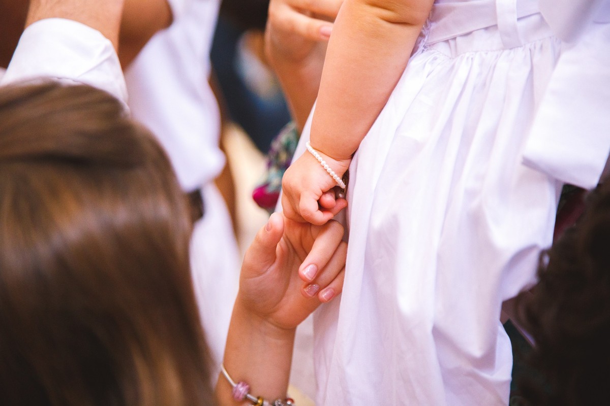 Detalhe de uma criança segurando a mão de uma bebê que está no colo.