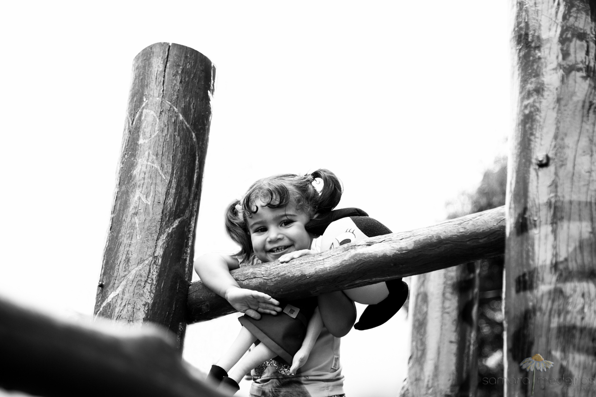 Foto em preto e branco de uma criança brincando e sorrindo em cima do brinquedo de madeira da Praça do Papa em Belo Horizonte.