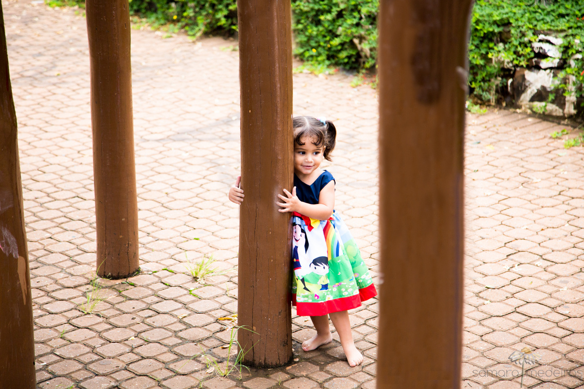 Criança brincando nas estruturas de madeira de um parquinho infantil em praça.