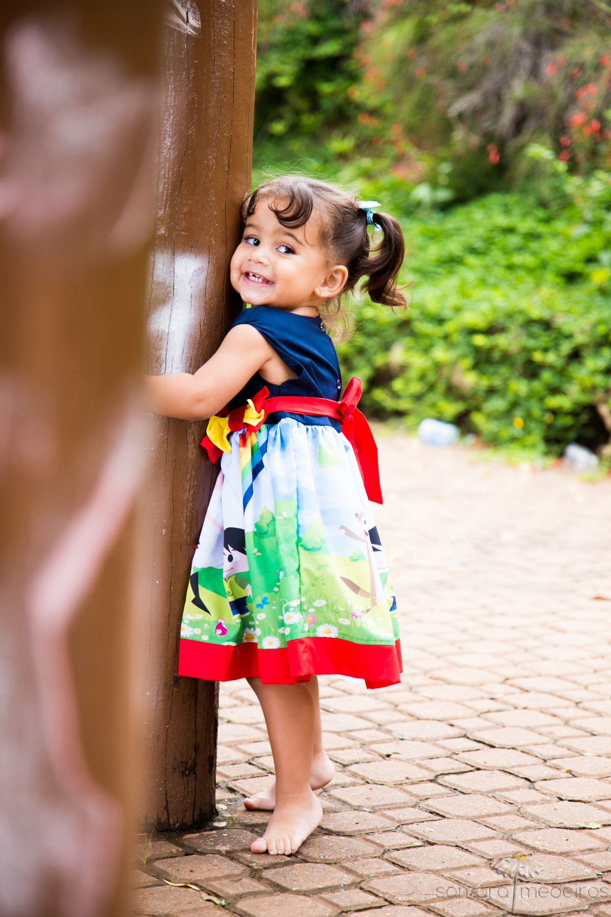 Criança brincando e fazendo careta, nas estruturas de madeira de um parquinho durante ensaio externo infantil.