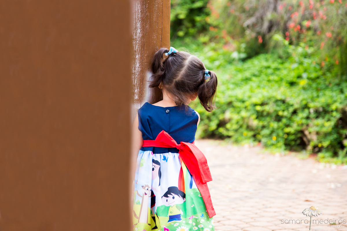 Criança de costas, brincando nas estruturas de madeira de um parquinho em praça de Belo Horizonte.