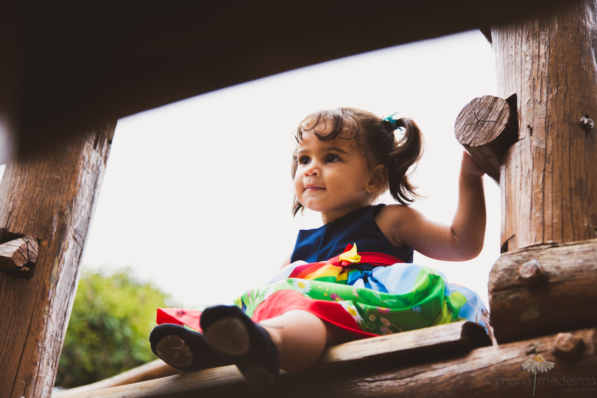Criança sentada em um parquinho de madeira na Praça do papa.