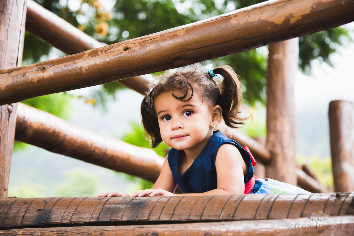 Criança deitada na estrutura de madeira de um parquinho infantil na Praça do Papa em Belo Horizonte.