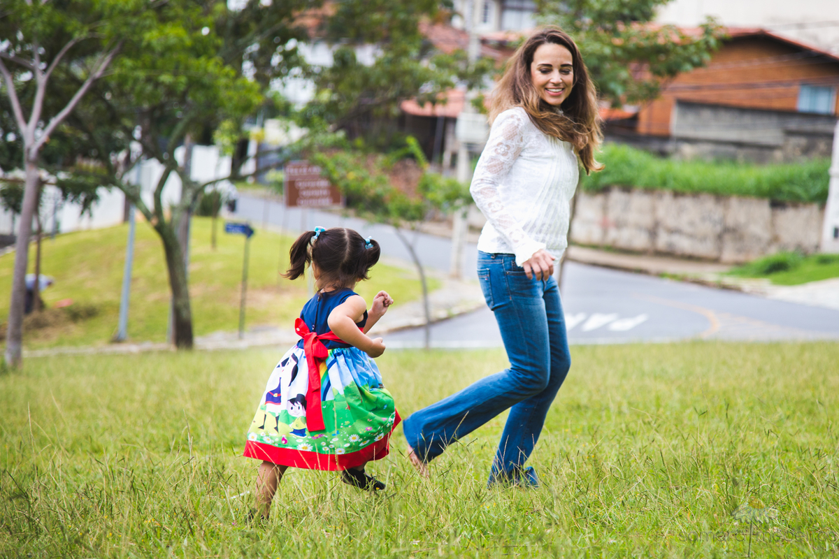 Criança e sua mãe correndo e brincando na grama em uma sessão de fotos externa em uma praça.
