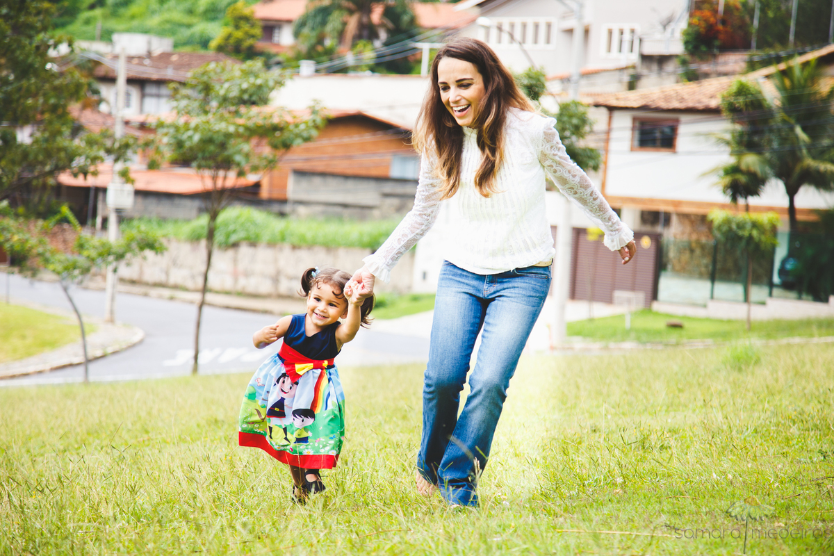 Criança e sua mãe correndo na grama, durante uma sessão de fotos em uma praça de Belo Horizonte.