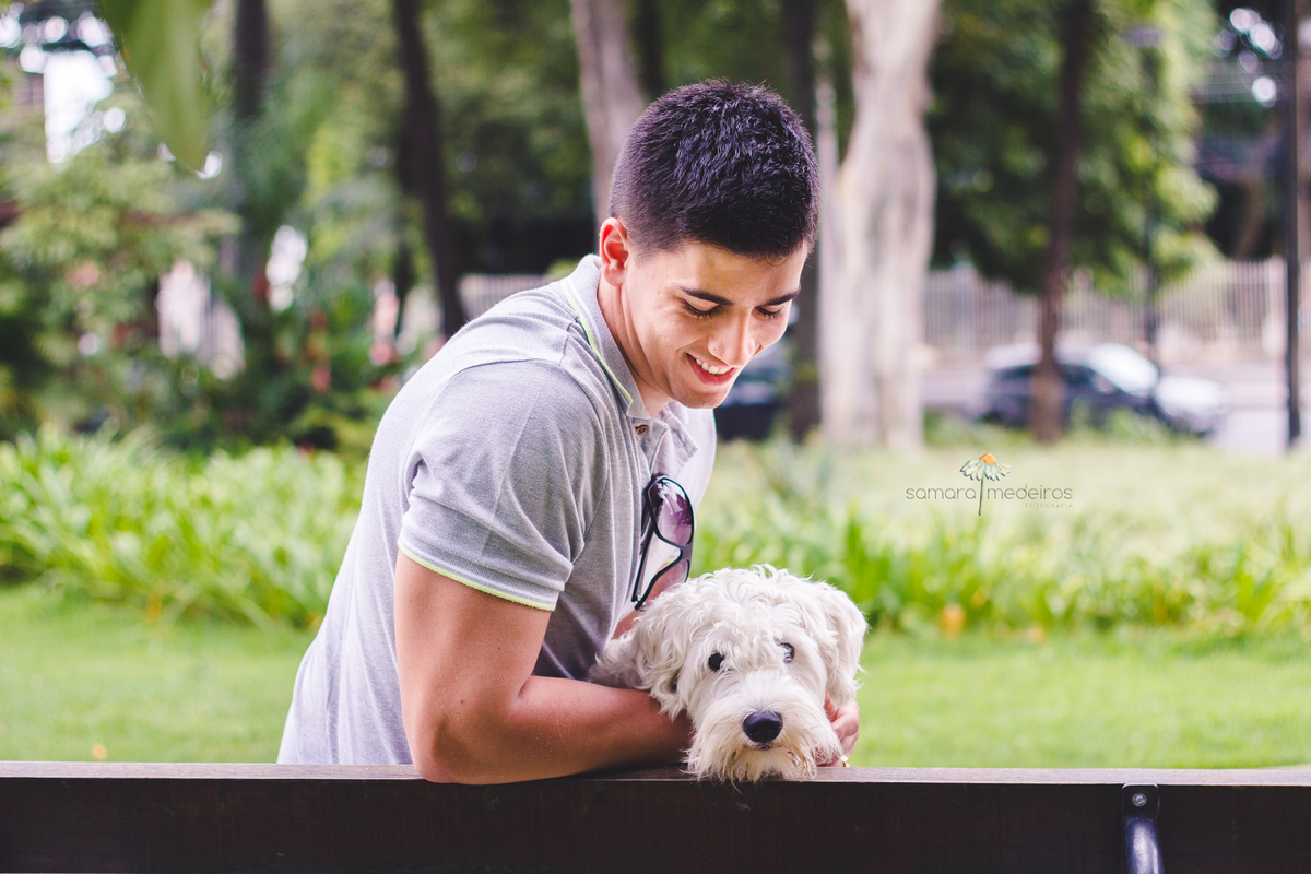 Cachorro e tutor sentados em um banco de praça, o cachorro olhando para a câmera e o tutor olhando o cachorro.
