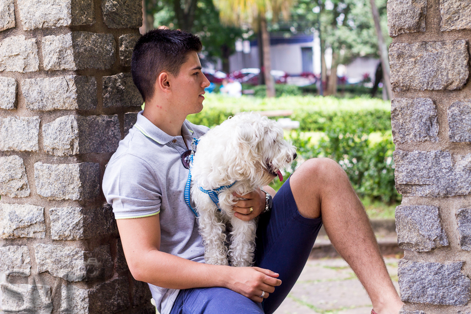 Foto urbana de um cachorro e seu tutor, sentados em uma construção de uma praça de Belo Horizonte.