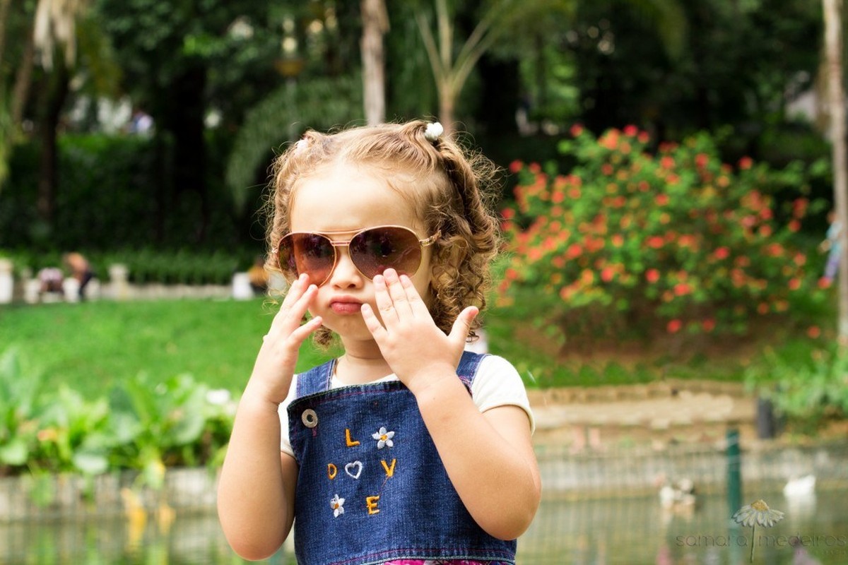 Criança posando com óculos de sol e fazendo careta.
