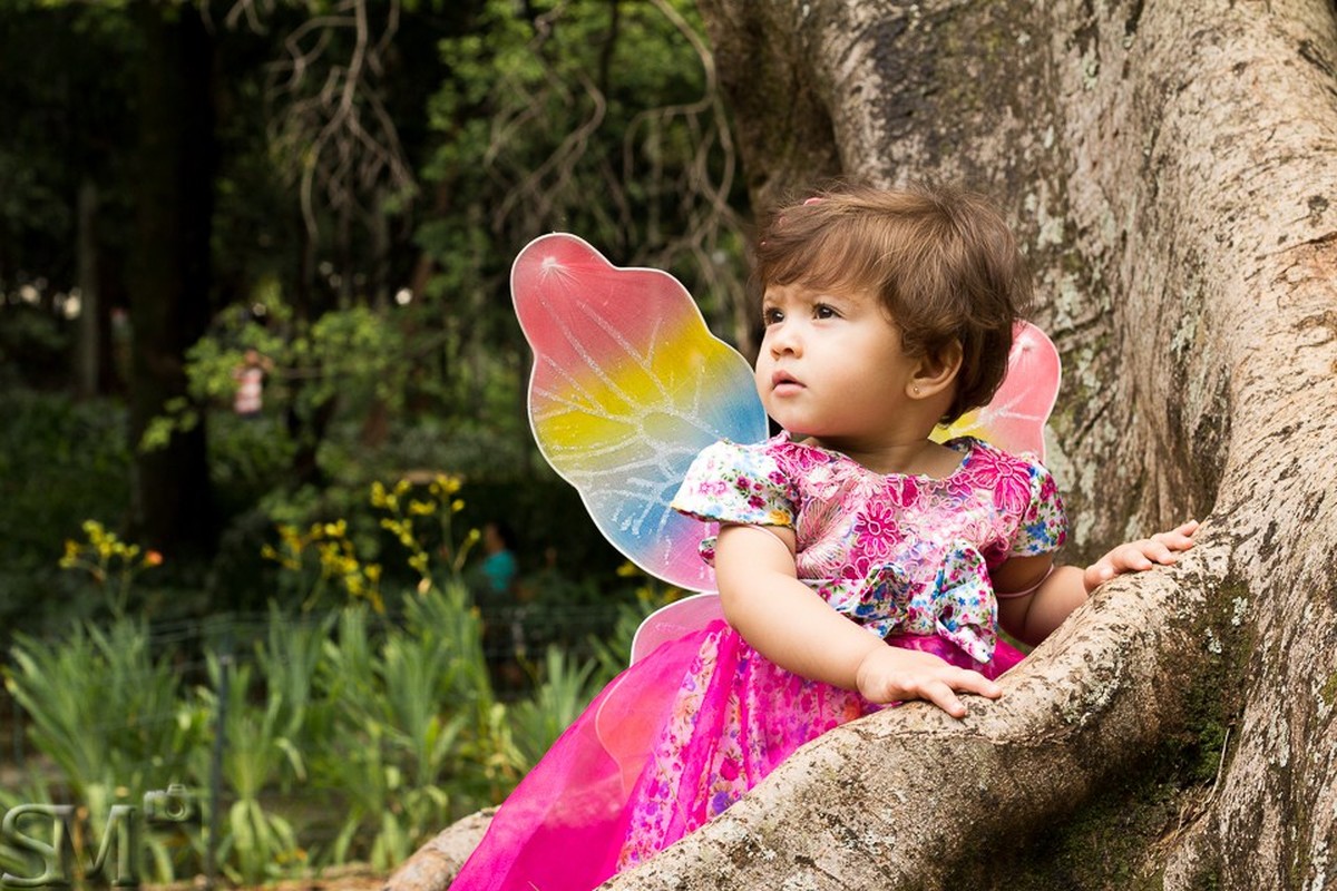 Criança com asas de fada apoiada em uma árvore em um parque em Belo Horizonte BH