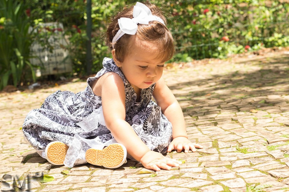 Criança sentada ao chão brincando, em ensaio externo em parque de Belo Horizonte.