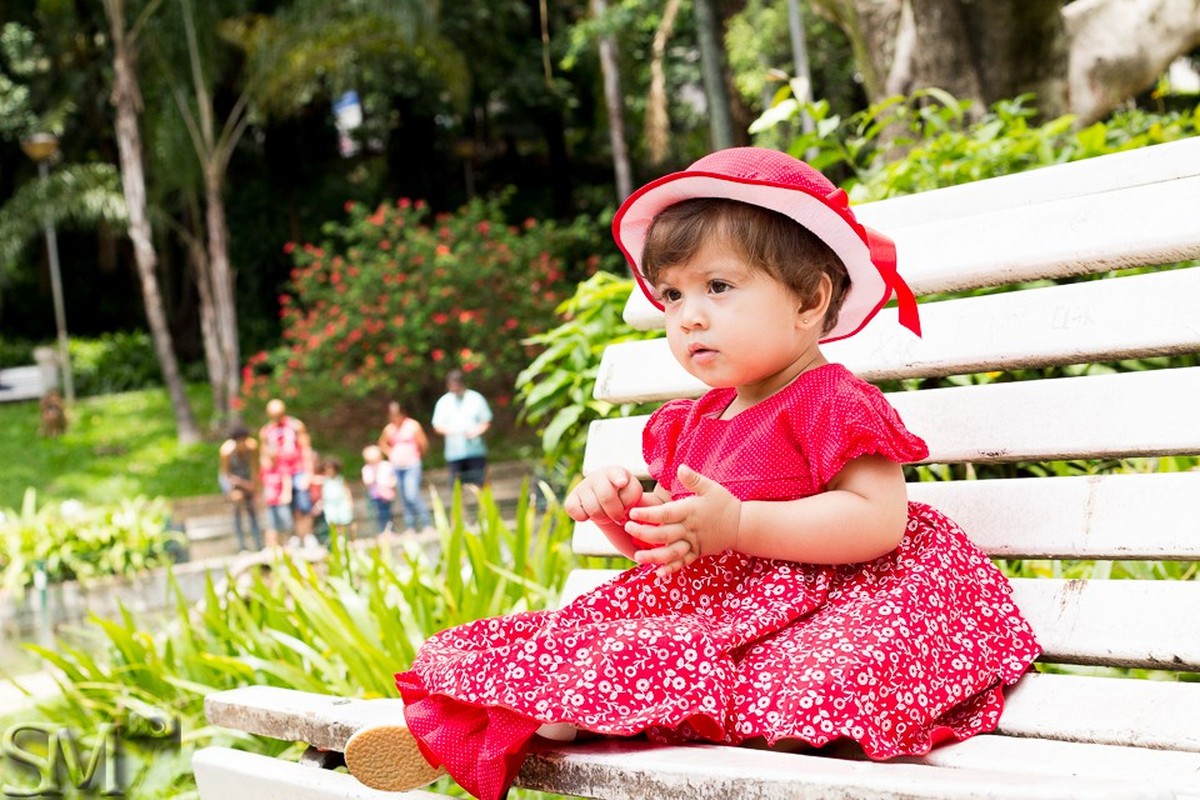 Criança sentada em um banco de praça em ensaio externo infantil feito em um parque de Belo Horizonte.