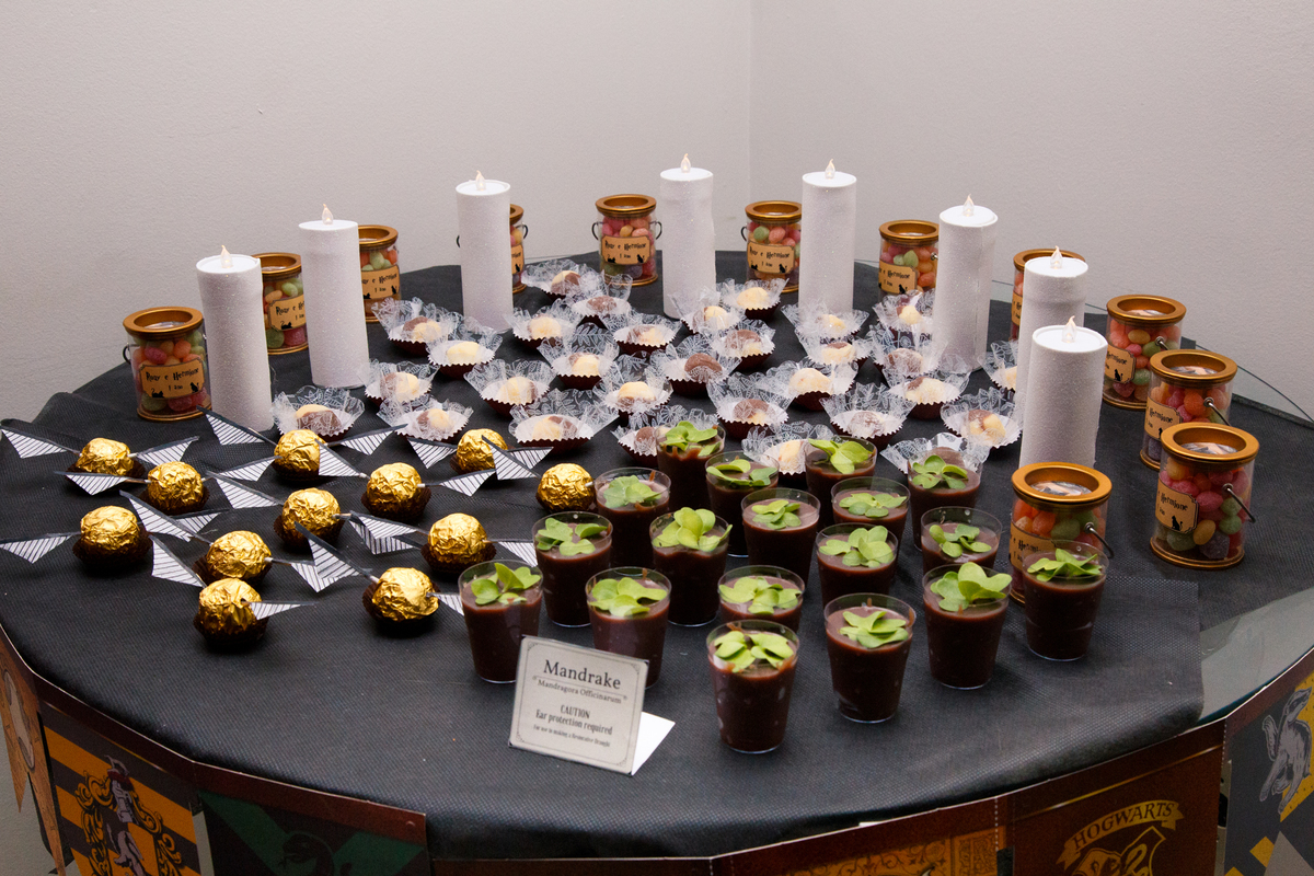 Decoração da mesa de doces em aniversário com tema Harry Potter, com mandrágoras, pomos de ouro e velas.