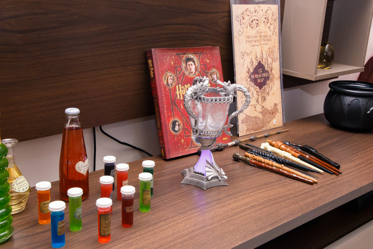Visão mais ampla da decoração de aniversário com tema Harry Potter com algumas poções, a taça tribruxo, varinhas e alguns livros no tema.