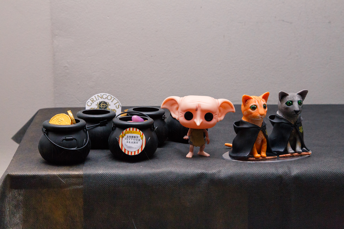 Detalhe da decoração da mesa do bolo em aniversário no tema Harry Potter, com figurinhas dos dois gatinhos, caldeirões com feijões de todos os sabores e um boneco do Dobby, elfo doméstico.