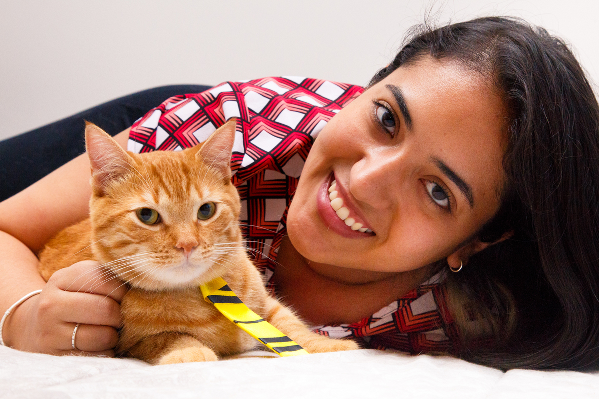 Tutora deitada na cama abraçando seu gatinho amarelo que usa uma gravata amarela da Lufa Lufa.