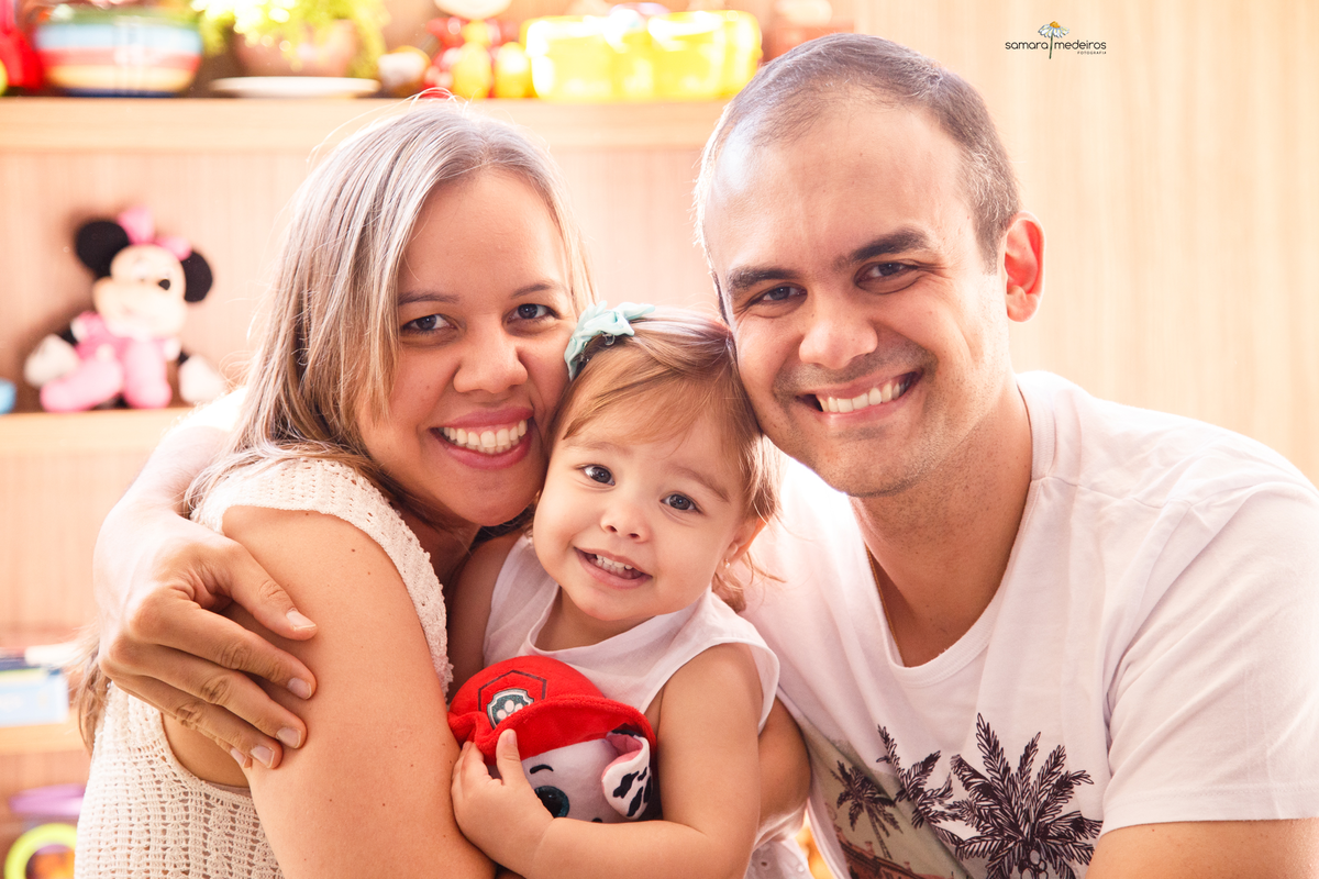 Retrato da família, com pai, mãe e bebê, todos se abraçando, olhando para a foto e sorrindo.