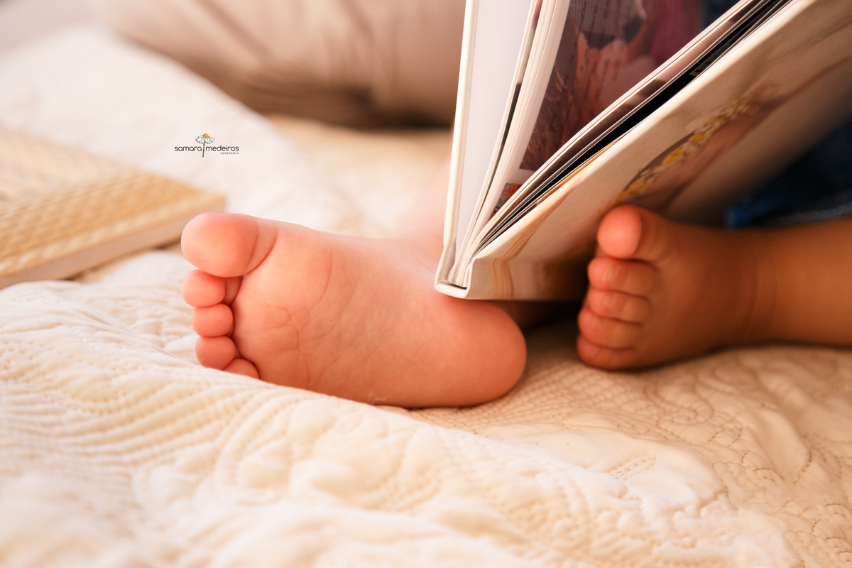 Foto em close dos pés de uma bebê com um álbum de foto em seu colo, aparecendo parcialmente na foto.