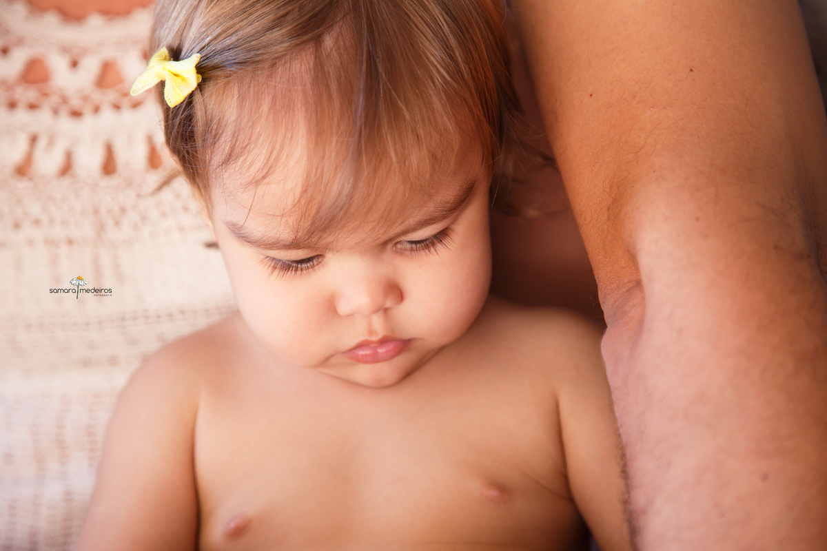 Close de uma bebê no colo da mãe olhando para baixo, para seu colo.