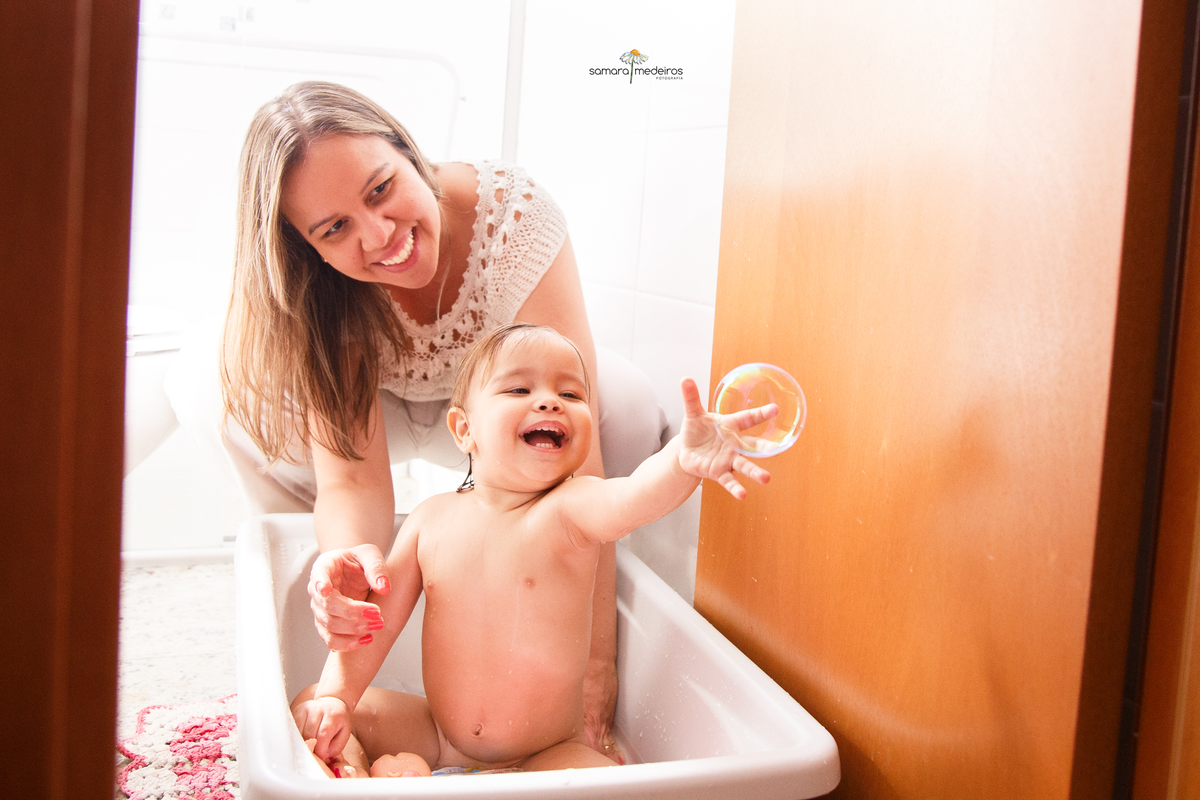 Bebê dentro de sua banheirinha tomando banho e brincando com bolhas de sabão.