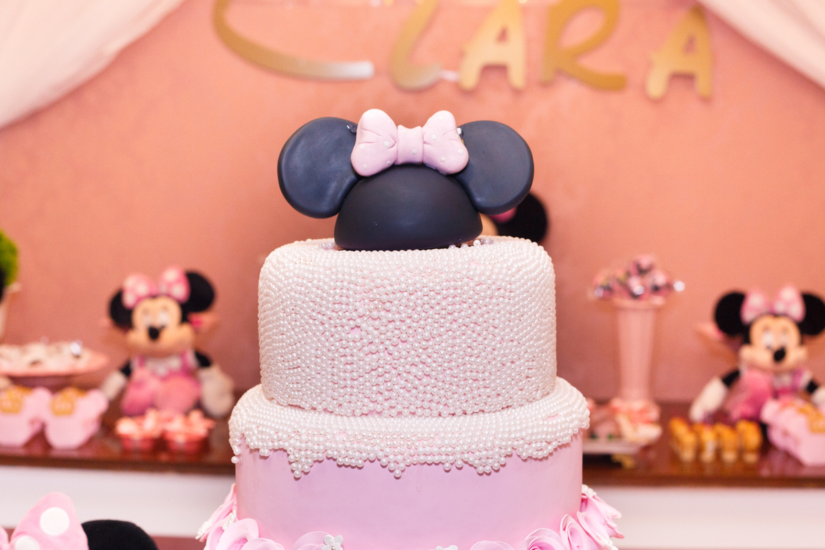 Detalhe do bolo cenográfico e topo do bolo de uma festa de aniversário infantil no tema Minnie, da Disney.