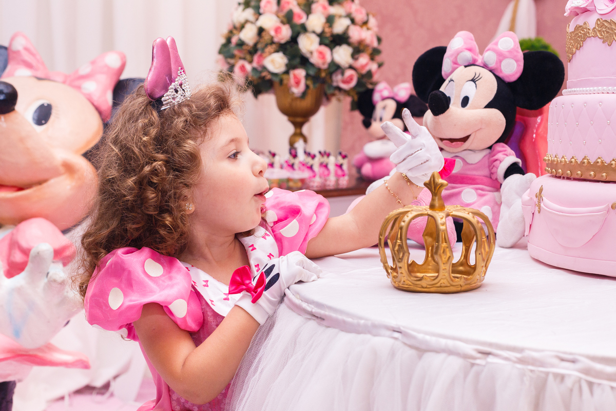 Criança em seu aniversário de 3 anos olhando a ponta do dedo após encostar no bolo cenográfico, na mesa de doces.