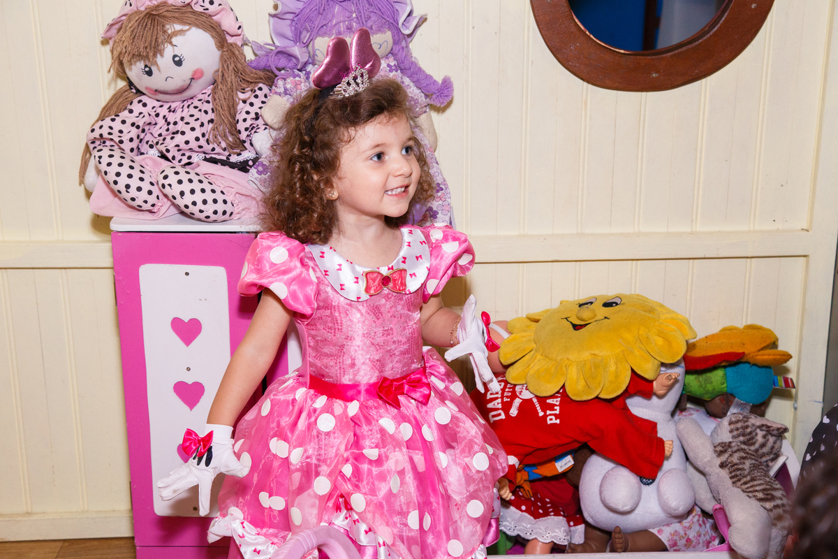 Criança com vestidinho da Minnie e um enorme sorriso dentro da casinha de brinquedo em um buffet de festa infantil, comemorando seu aniversário de 3 anos.