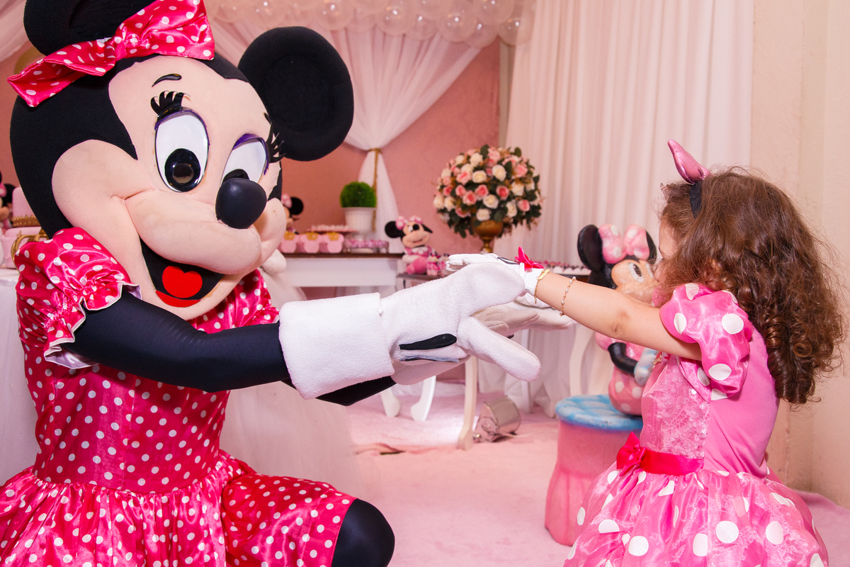 Foto da criança em seu aniversário infantil junto com a personagem animada Minnie, de mãos dadas dançando.