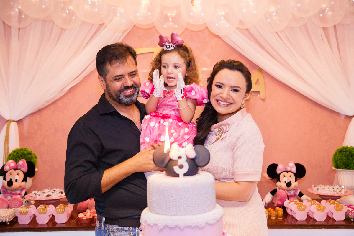 Família reunida atrás do bolo na hora do parabéns em aniversário infantil do tema Minnie.